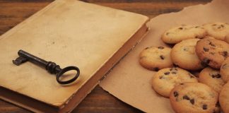 Photograph of a beige book with a black iorn key on it next to a piece of paper with cookies piled on it