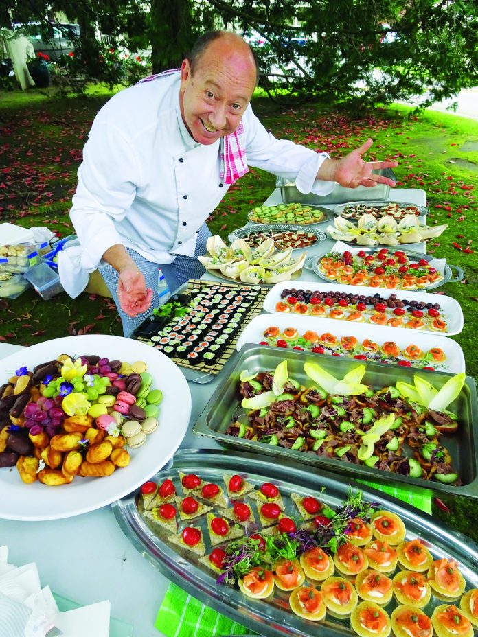 A photograph of chef Stephen Wilson leanind over a table laden with food