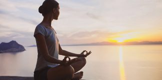 woman sitting in meditation pose with the sea and sunset in the background