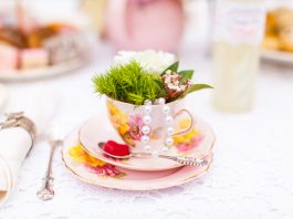 Photograph of a pink teacup and saucer that is filled with green leaves on a white table cloth