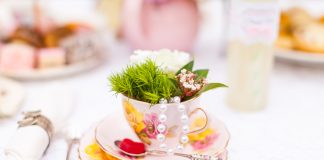 Photograph of a pink teacup and saucer that is filled with green leaves on a white table cloth