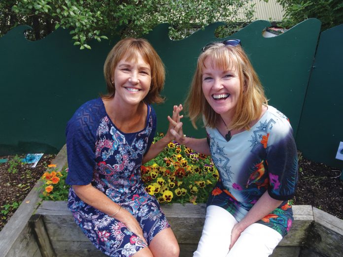 Photograph of two women sitting on a planter box at the Children's Garden preschool