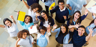 A group ofd school children looking up at the camera and holding up their essays