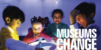 A group of children standing around a table with the caption Museums change lives