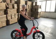 a woman sitting on an e-bike in a warehouse in front of cardboard boxes along one wall