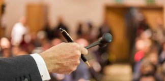 picture of a hand holding a gavel in front of a room of people