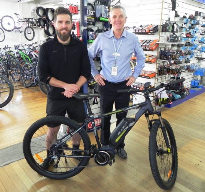 Two men standing next to each other with an e bike