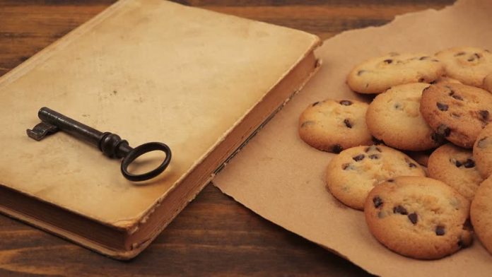 Photograph of a beige book with a black iorn key on it next to a piece of paper with cookies piled on it