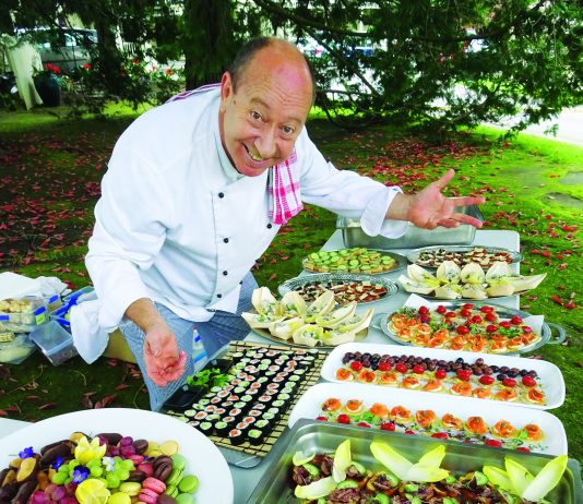 A photograph of chef Stephen Wilson leanind over a table laden with food