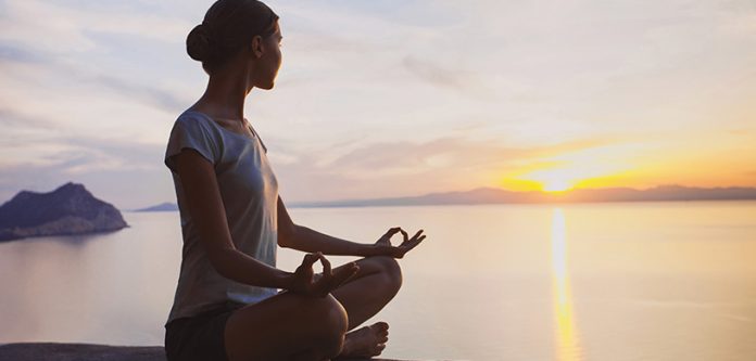 woman sitting in meditation pose with the sea and sunset in the background
