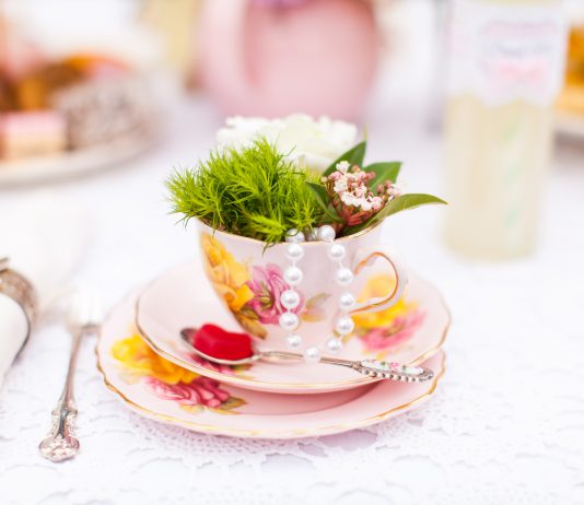 Photograph of a pink teacup and saucer that is filled with green leaves on a white table cloth