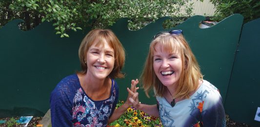 Photograph of two women sitting on a planter box at the Children's Garden preschool