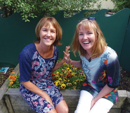 Photograph of two women sitting on a planter box at the Children's Garden preschool