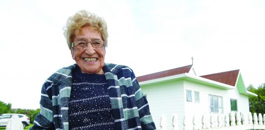 photograph of Dene Reweti (92) standing in front of the all saints church