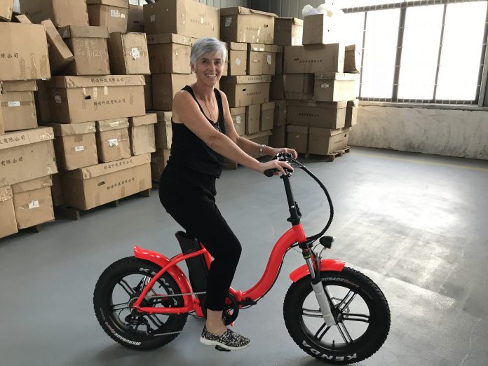a woman sitting on an e-bike in a warehouse in front of cardboard boxes along one wall