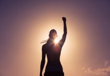 a silhouette of a woman standing in front of the sun with her arm raised over her head