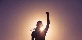 a silhouette of a woman standing in front of the sun with her arm raised over her head