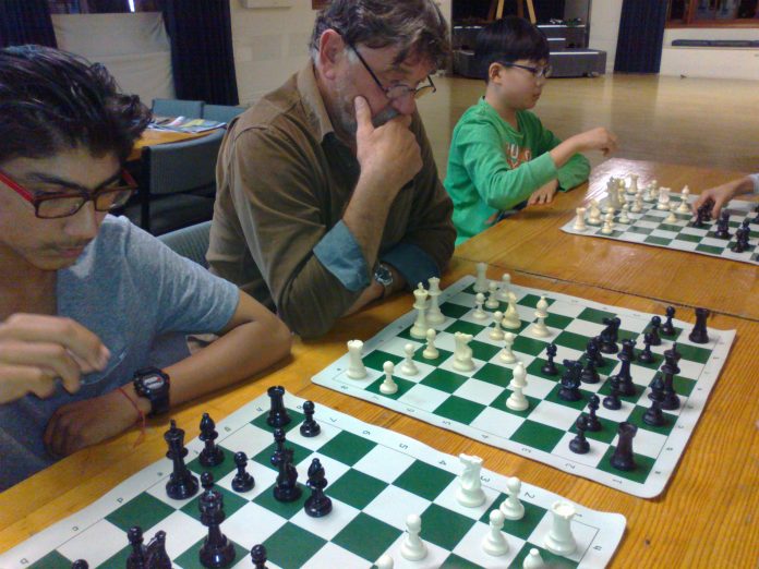 three people sitting in a row playing three different games of chess
