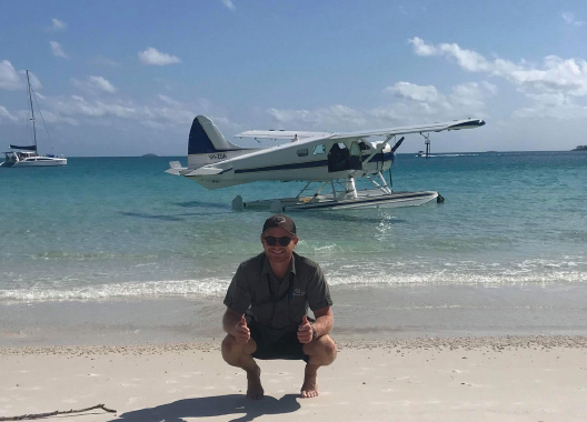 picture of a man on a beach with a seaplane behind him on the water